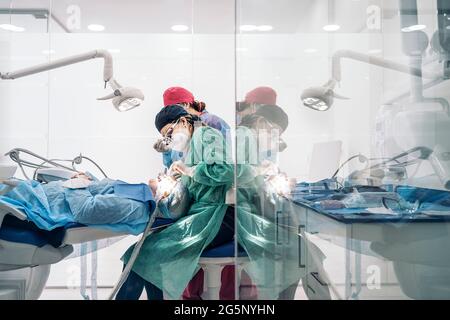 Dentists wearing face mask and protective clothes working in modern bright clinic. Stock Photo