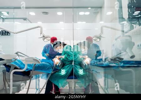 Dentists wearing face mask and protective clothes working in modern bright clinic. Stock Photo