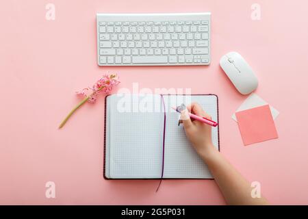 Pink work desk with female hand writes notes in notebook at workplace. Desktop office space top view. Work space girly office table. Back to school Stock Photo