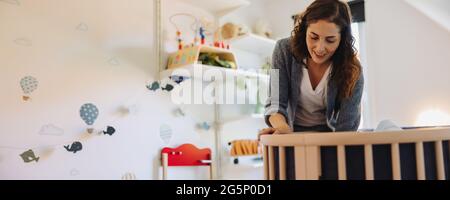 Mom training her baby to sleep in a crib. Woman admiring their baby in crib. Stock Photo