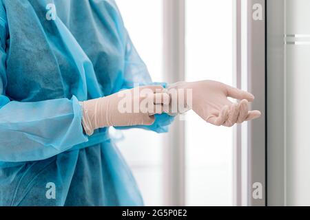 Medical worker wearing face mask and protective clothes putting on latex gloves. Stock Photo