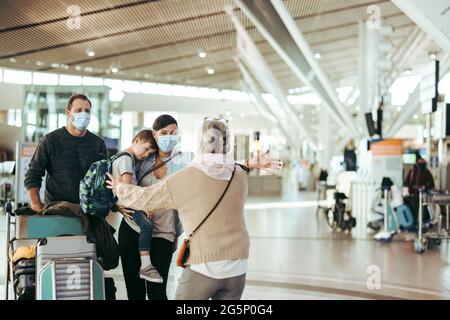 Senior woman welcoming her daughter and family  with open arms at airport arrival gate. traveler family of three welcomed by grandma at airport in pan Stock Photo