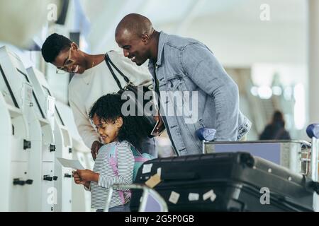 African family looking at the boarding pass in hands of their daughter at airport. Young girl looking happy to hold air ticket print while standing wi Stock Photo