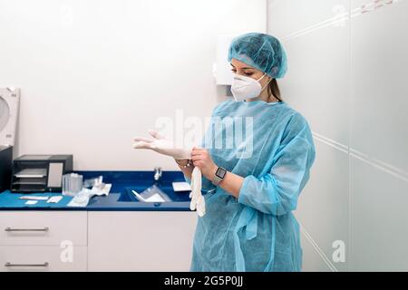 Female medical worker wearing face mask and protective clothes putting on latex gloves. Stock Photo