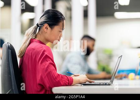 Focused asian woman sitting in her desk in the office and working with her laptop. Stock Photo