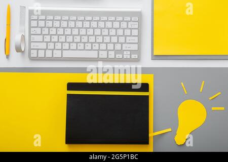Yellow light bulb idea metaphor on desktop with keyboard pc computer and suppliers in workspace on gray table background. Stock Photo