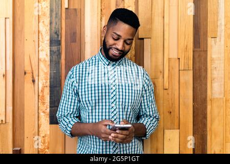 Young black business man using his mobile phone and standing against wooden background. Stock Photo