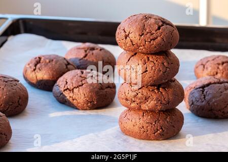 Baked cracked round chocolate cookies piled up on top of each other on a baking sheet with parchment paper just taken out of the oven. Tea or coffee s Stock Photo