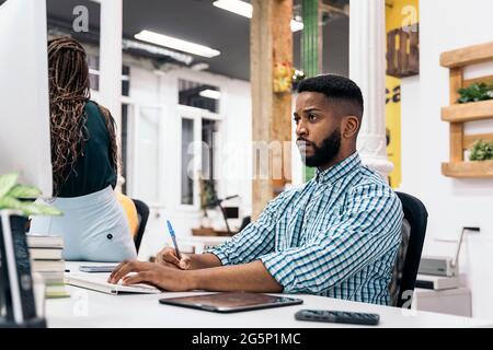Afro american office worker sitting in his desk and using his laptop. He is concentrated and looking the screen. Stock Photo