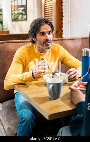 Boomer man eating lunch with his coworkers in the office kitchen and talking. Co-working concept. Stock Photo