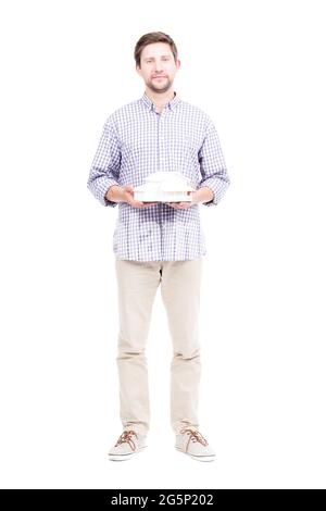 Studio portrait shot of handsome bearded Caucasian man wearing casual clothes holding house model in hands, white background Stock Photo