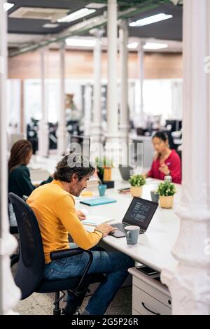 Multicultural teamwork sitting in big desk and using laptops in a modern bright office. Co-working concept Stock Photo