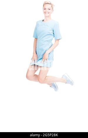 Vertical full length studio shot of joyful Caucasian woman with blond hair wearing blue dress jumping, white background Stock Photo