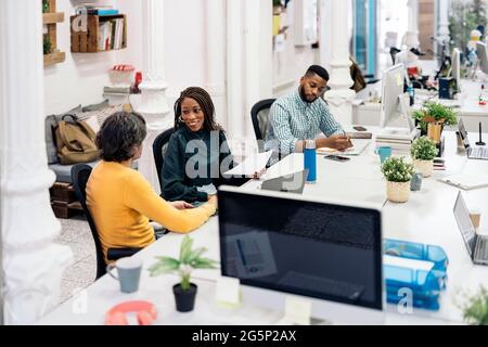 Happy diverse work team sitting in big desk and doing paper work. Co-working concept. Stock Photo