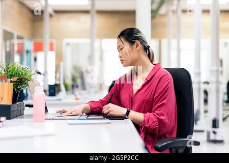 Focused asian woman sitting in her desk in the office and working with her laptop. Stock Photo
