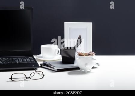 White table with laptop for remote work or study. Black laptop with blank display layout template on black background. Office pc desk workspace in Stock Photo