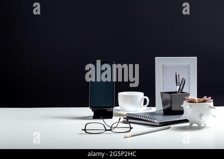Office or home Office workspace. Desktop with smart phone template blank, notepads pens office suppliers cup of coffee drink plant flower. White work Stock Photo