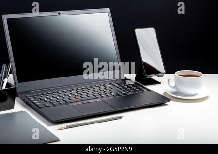 Desktop with laptop pc, office suppliers. Home Office laptop blank template display workspace with cup of coffee. White work desk table on black Stock Photo
