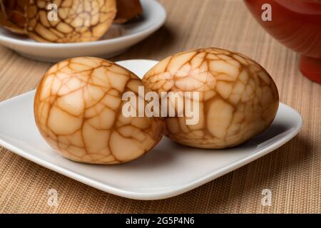 Pair of traditional Chinese herbal tea eggs on a plate as snack food close up and eggshell in the background Stock Photo