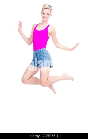 Vertical full length studio portrait of cheerful young Caucasian woman wearing summer outfit jumping, white background Stock Photo