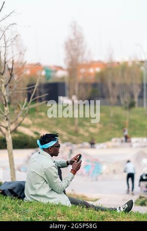 Cool young african man sitting in the grass and using his mobile phone. Stock Photo