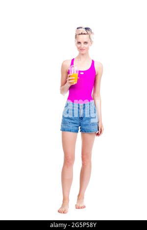 Vertical full length studio portrait of modern young Caucasian woman wearing summer outfit drinking fresh orange juice, white background Stock Photo