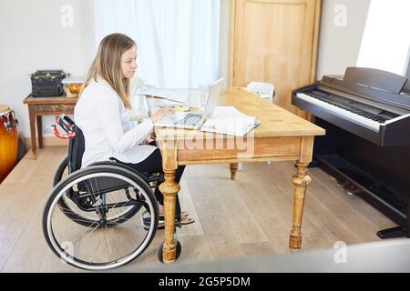 Paralyzed business woman in wheelchair working on laptop computer online in home office Stock Photo