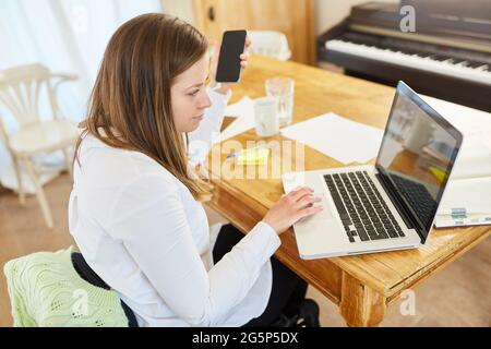 Paralyzed woman in wheelchair using laptop computer online at table in living room as home office Stock Photo