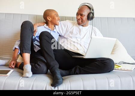 Father using laptop computer on the sofa during childcare with his son in the home office Stock Photo