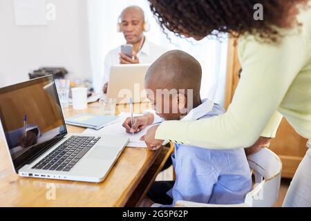 Mother helping son with distance learning on PC with father doing video conference online in the background Stock Photo
