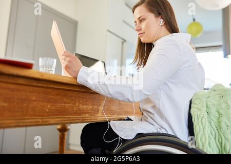 Woman in wheelchair on tablet computer at home in the home office during a video conference online Stock Photo
