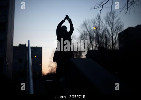 The silhouette of a girl taking a photo of the evening sky. A girl walks at night in the street. Stock Photo