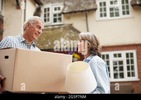 Mature Couple Carrying Boxes On Moving Day In Front Of Dream Home Stock Photo
