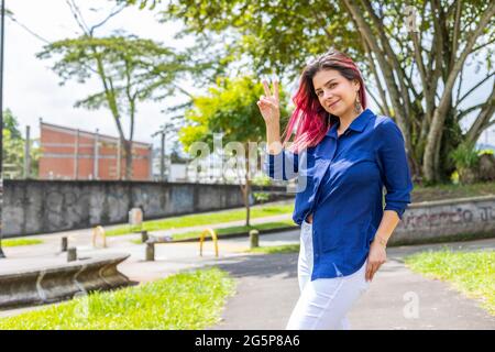 young stylish woman in outdoors doing peace sign with her right hand Stock Photo