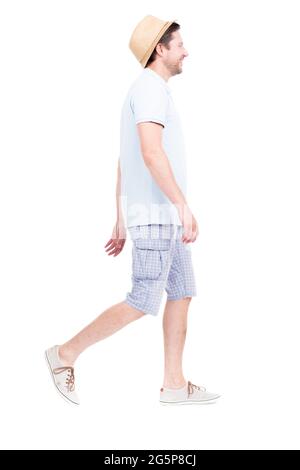 Vertical full length side view portrait of handsome bearded Caucasian man wearing summer outfit with hat walking somewhere, white background Stock Photo