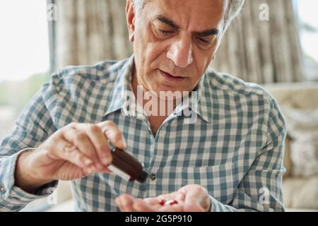 Mature Man Sitting On Sofa At Home Taking Medication Stock Photo
