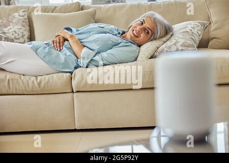 Woman Lying On Sofa Asking Digital Assistant Or Smart Speaker Question Stock Photo