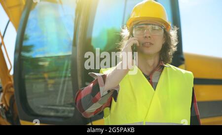 Excavator operator in hard hat talking by smartphone. Stock Photo
