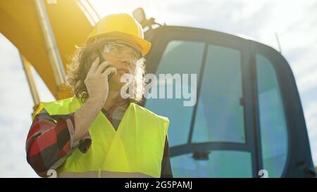 Excavator operator in hard hat talking by smartphone. Stock Photo