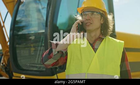 Excavator operator in hard hat talking by smartphone. Stock Photo
