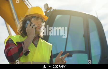Excavator operator in hard hat talking by smartphone. Stock Photo