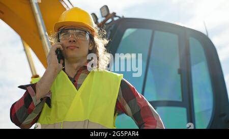 Excavator operator in hard hat talking by smartphone. Stock Photo