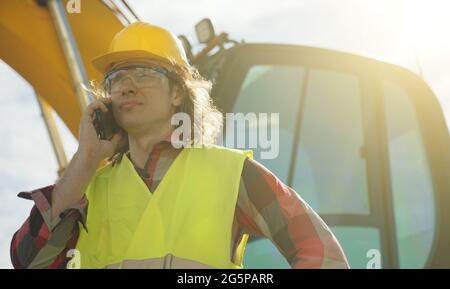 Excavator operator in hard hat talking by smartphone. Stock Photo