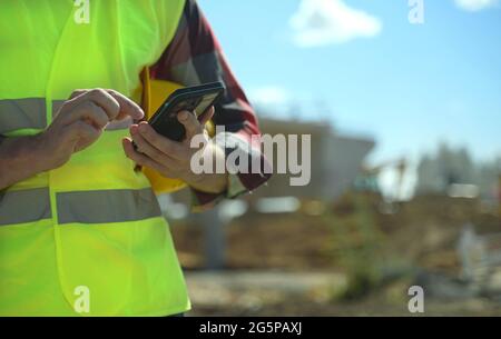 Builder with hard hat and high vis jacket using smartphone. Close-up. Stock Photo
