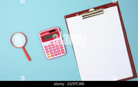 pink calculator, folder with blank white sheets and black magnifier on a blue background, top view Stock Photo