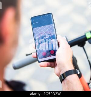 Close up of hand and smartphone, unlocking dockless electric scooter for rent with debranded generic phone app. Stock Photo