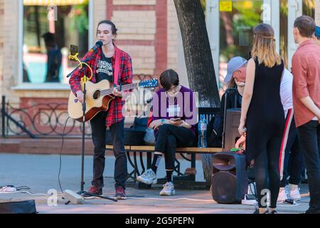 A young guy stands with a guitar on a central street, plays and sings, earning money. Chelyabinsk, Russia, May 17, 2021 Stock Photo