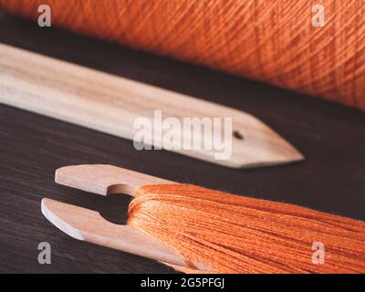 Weaving shuttle, pickup stick and orange thread on spool. Equipment for manual weaving, close up Stock Photo