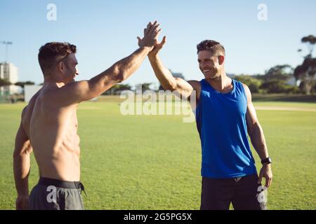 Two happy caucasian muscular men exercising outdoors, smiling and high fiving Stock Photo