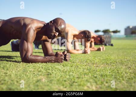 Diverse group of muscular men exercising doing planks outdoors Stock Photo